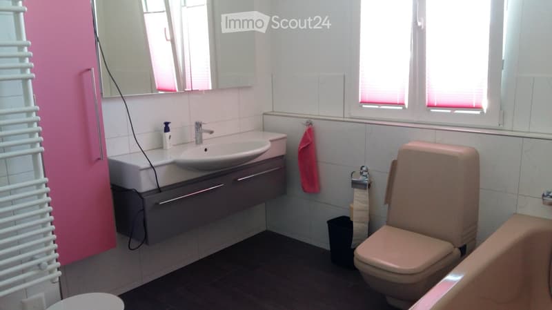 Modern bathroom with a sink, mirror, toilet, bathtub, and a towel hanging on the wall. The room features white tiles, a dark floor, and a radiator on the left side.