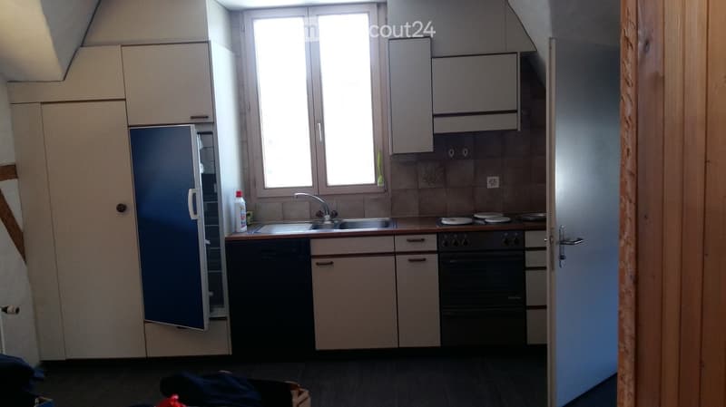 Compact kitchen with light-colored cabinets, a stainless steel sink, a refrigerator, and an oven. The space features two windows and a small countertop area.