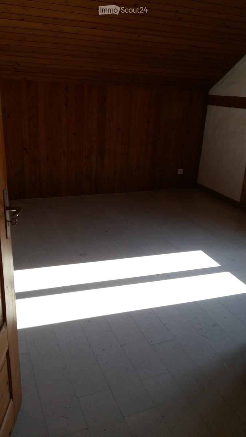Empty room with wooden walls and ceiling, concrete floor, and a large window allowing natural light to enter.