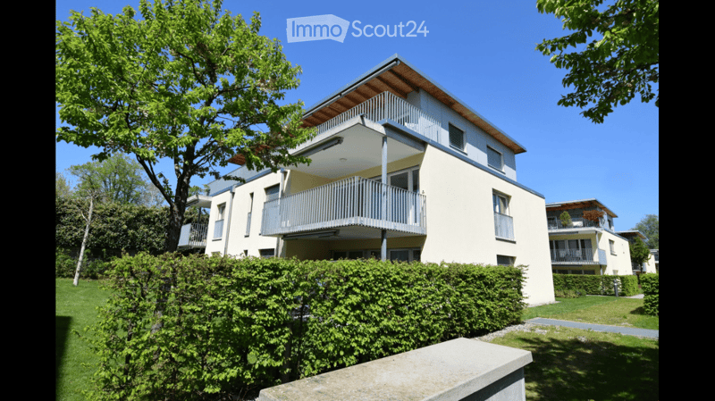 Modern two-story residential building with balconies, surrounded by greenery and a well-maintained lawn.