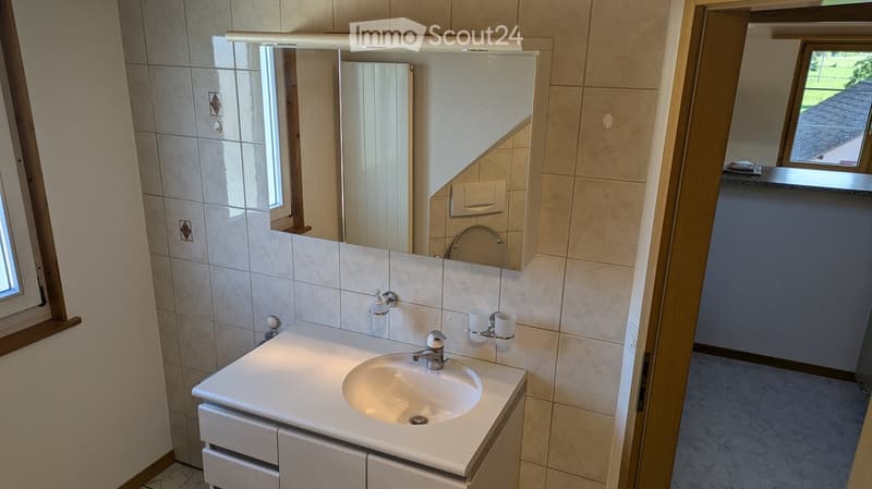 Modern bathroom with a white sink, chrome faucet, large mirror, and tiled walls. Features include a soap dispenser, two cups, and a window providing natural light.