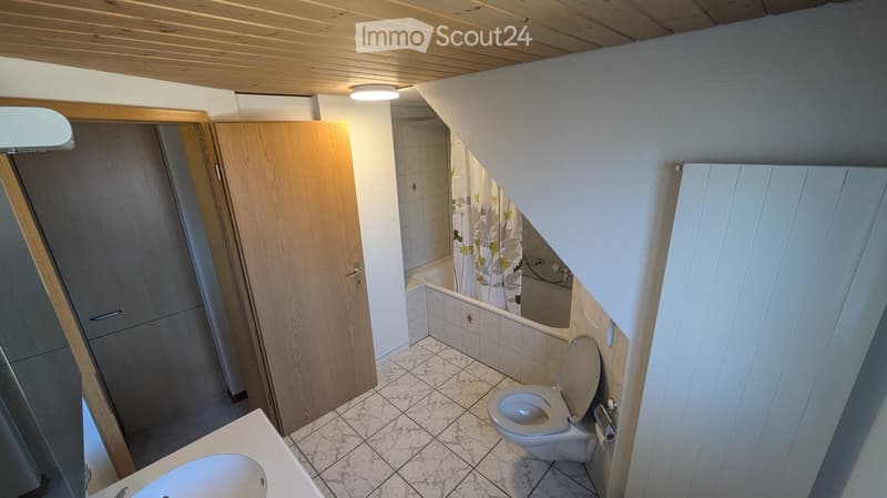 Bathroom with a toilet, sink, and bathtub. The room features tiled walls and a wooden door leading to another area.