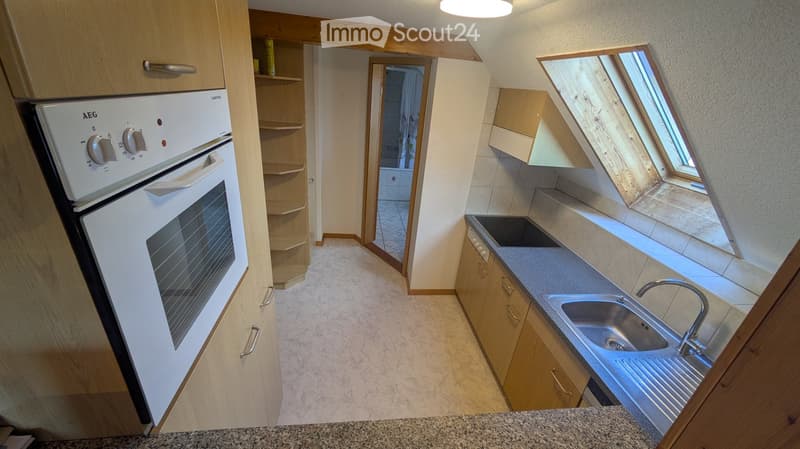Modern kitchen with light wooden cabinets, a white oven, a stainless steel sink with a modern faucet, and a countertop. The space features a skylight window and a view into an adjacent bathroom.