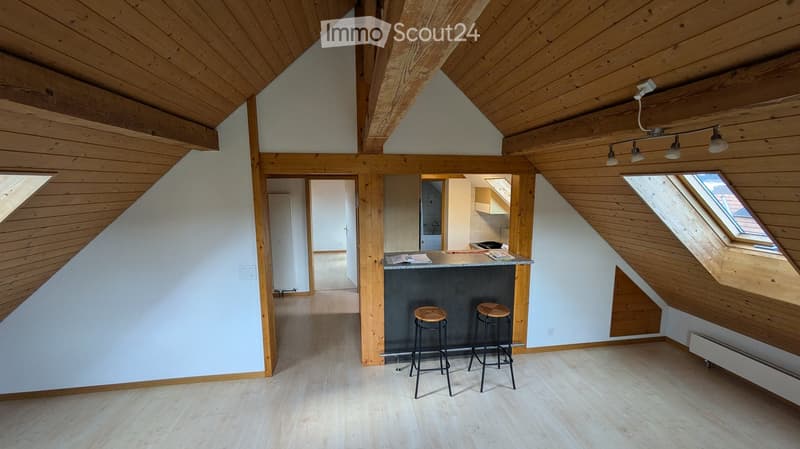 Loft-style room with wooden beams, exposed ceiling, bar counter, two stools, and modern lighting.