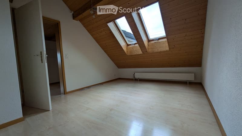 Empty attic room with wooden slanted ceiling, skylights, light-colored wooden flooring, and white walls.