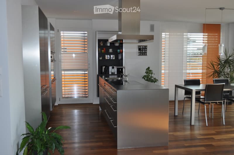 Modern kitchen with a central island, stainless steel appliances, wooden flooring, and a dining area with a table and chairs.