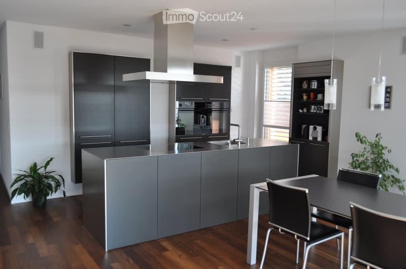 Modern kitchen with dark grey cabinets, a central island, built-in appliances, and a dining area with a table and chairs.