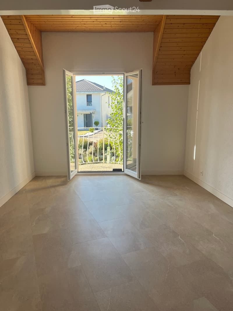 Empty room with tiled floor and large sliding glass doors leading to a patio area. The ceiling has wooden beams and the walls are painted white.