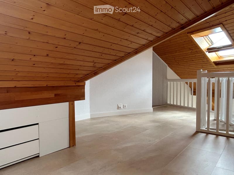 Empty attic space with wooden ceiling, tiled floor, white walls, and a skylight window. Features a white baby gate and a built-in storage unit with drawers.