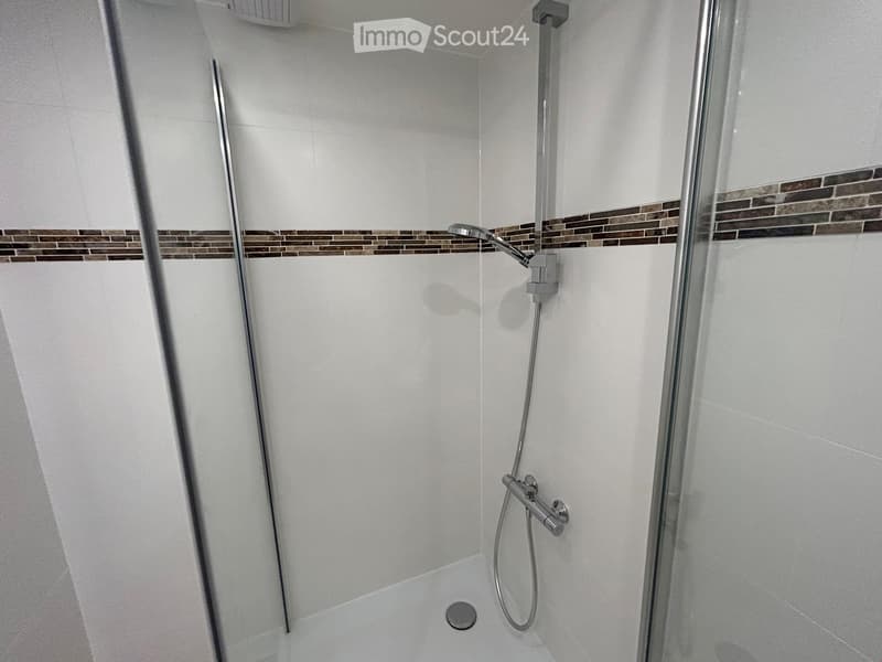 Modern shower stall with white tiles, a glass enclosure, and a sleek chrome showerhead and faucet.