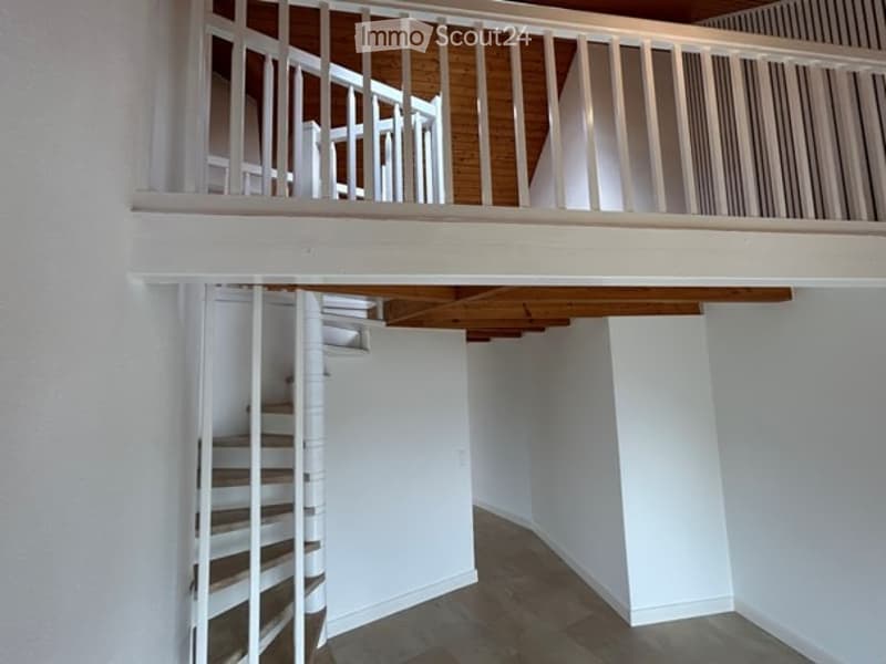 Spiral staircase leading to an upper level with white railings and wooden beams, white walls, and a tiled floor.