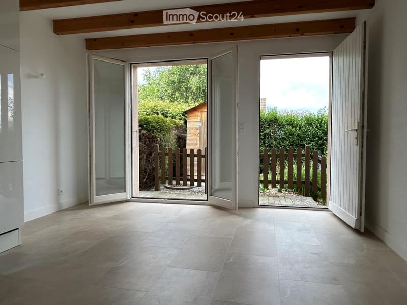 Bright, open hallway with large sliding glass doors leading to a garden, tiled floor, and exposed wooden beams on the ceiling.