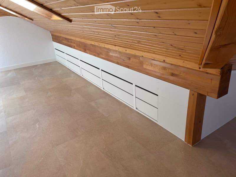 Empty room with wooden ceiling beams, white built-in storage units, and tiled floor.