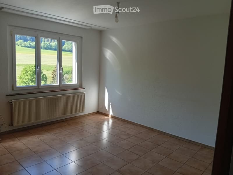 Empty room with tiled floor, white walls, large windows, radiator, and natural light from outside.