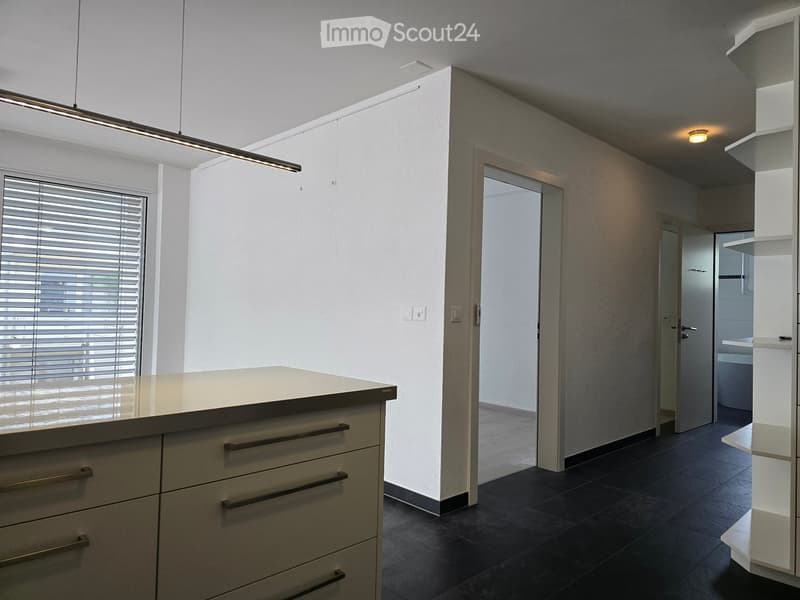 Modern kitchen with a central island, built-in cabinets, and sleek lighting fixtures. The space features dark tiled flooring and white walls.
