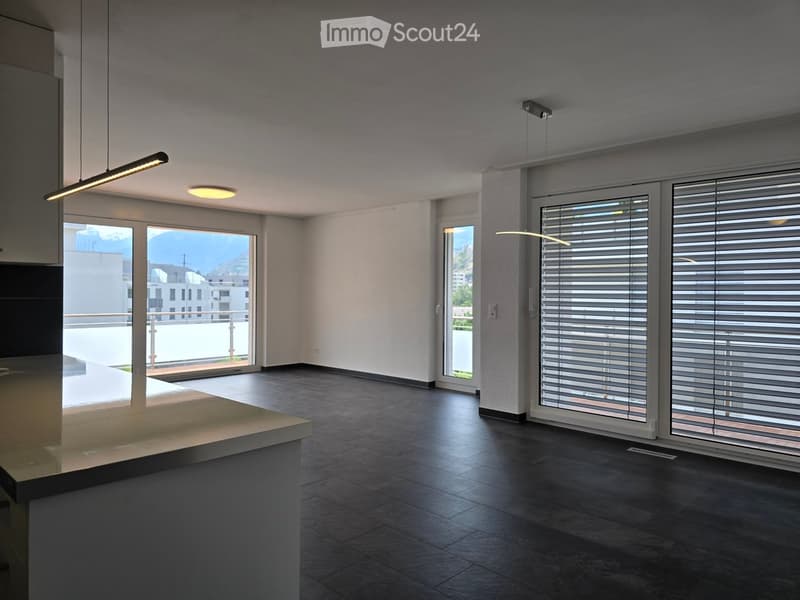 Empty room with dark tiled floor, white walls, large windows with blinds, and a small counter area.
