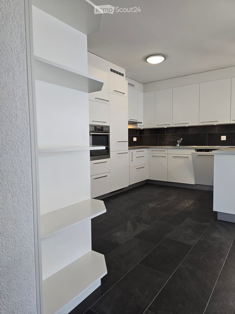 Modern kitchen with white cabinets, black tiled floor, built-in oven, and sink area.