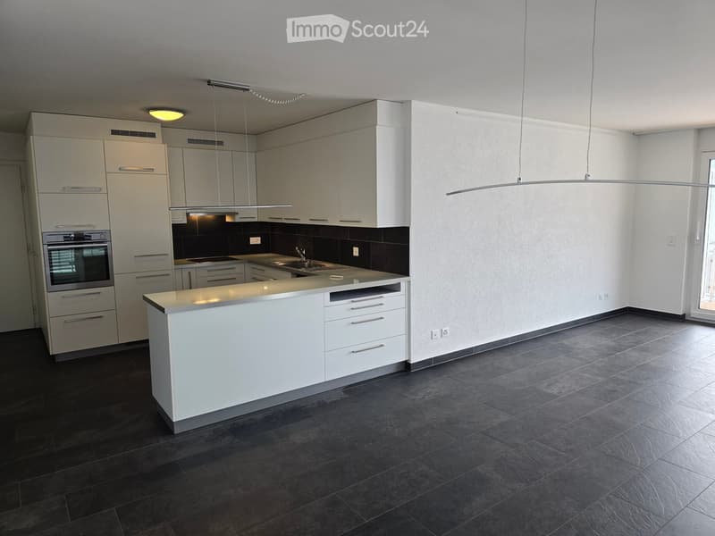 Modern kitchen with white cabinets, a central island, dark tiled floor, and built-in appliances including an oven and sink.