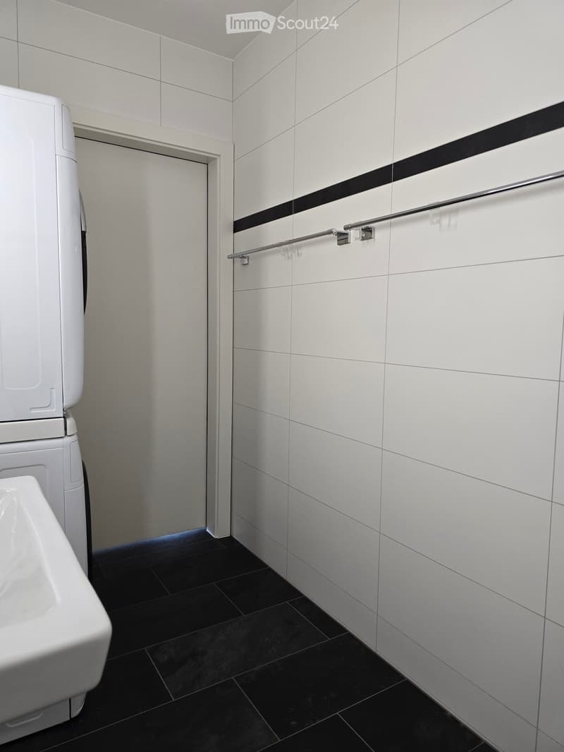 Modern bathroom with white tiled walls, black tiled floor, toilet, urinal, and towel rack.
