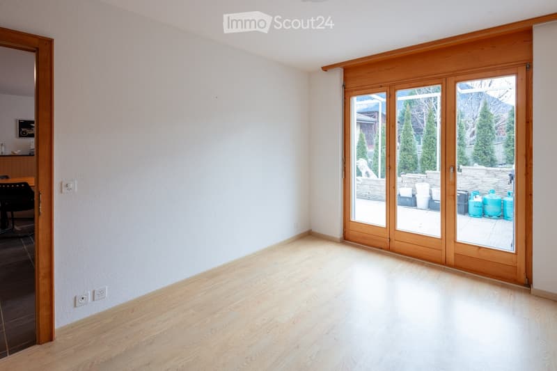 Empty room with light wooden flooring, white walls, and large sliding glass doors leading to an outdoor area.