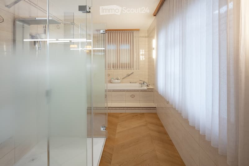 Modern bathroom with a bathtub, glass-enclosed shower, and wooden flooring.