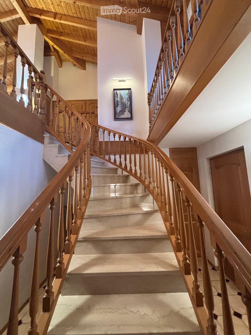 Spiral staircase with wooden handrails and balusters, beige walls, and a framed picture on the wall.