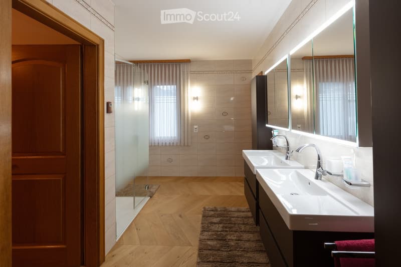Modern bathroom with double sinks, large mirror, wooden floor, and glass-enclosed shower area.