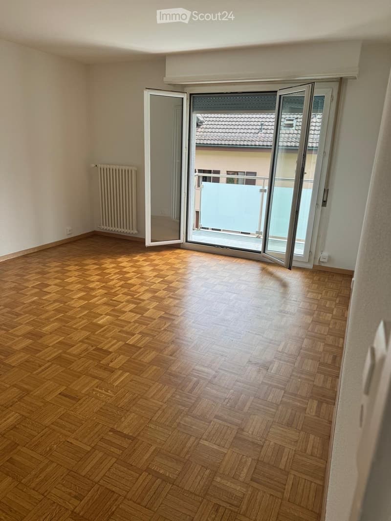 Empty room with wooden herringbone flooring, white walls, and large sliding glass doors leading to a balcony.