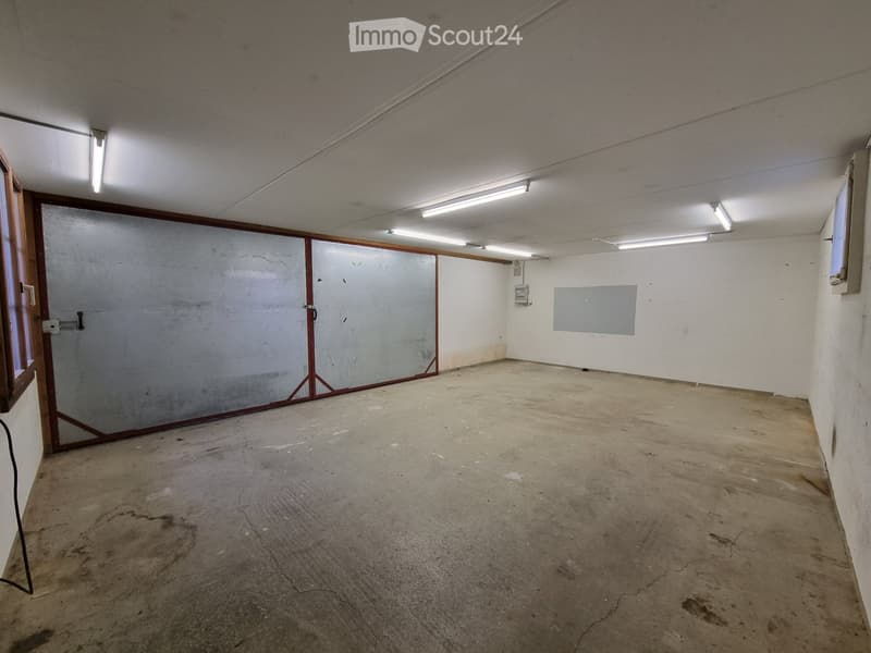 Empty room with concrete floor, metal doors, white walls, windows, and ceiling lights