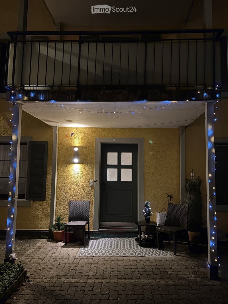 Balcony with a covered entrance, decorated with string lights, a small table with a Christmas tree, chairs, and potted plants.