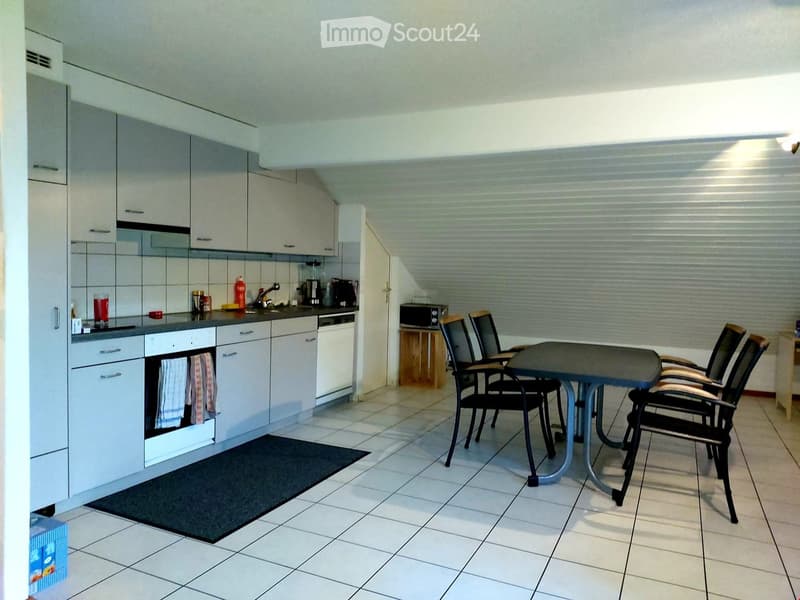 Modern kitchen with white cabinets, tiled floor, and a small dining area with a table and chairs. Appliances include an oven, dishwasher, and microwave. A blender and other small items are on the counter.