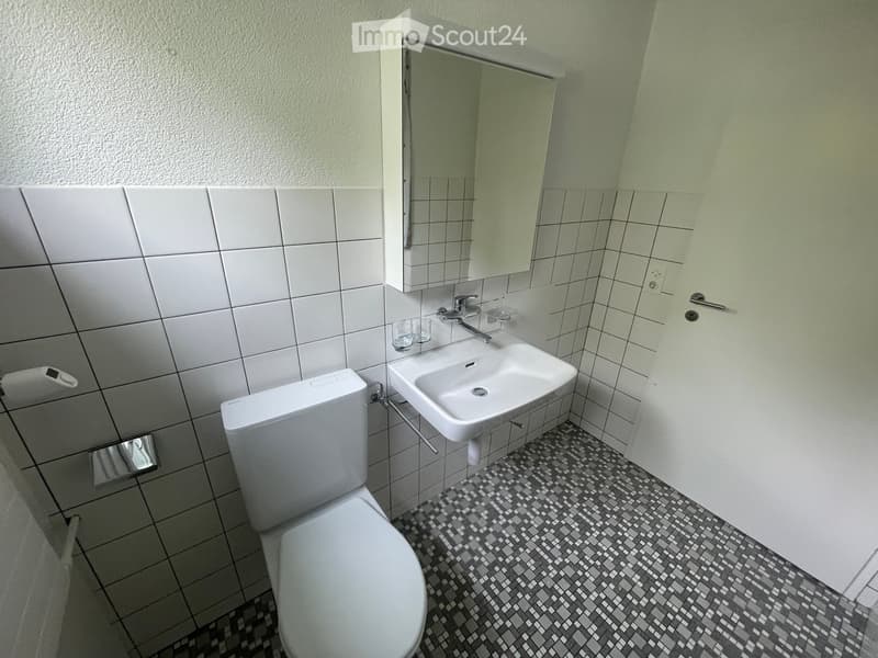 Modern bathroom with white tiles, a toilet, a sink with a faucet, a mirror, and a cup on the sink counter.