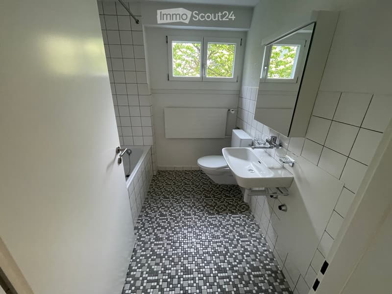 Modern bathroom with a bathtub, toilet, sink, and mirror. The walls are tiled, and the floor features a mosaic tile pattern.