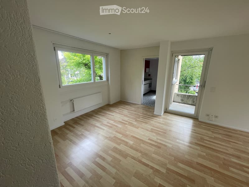 Empty room with wooden flooring, large windows, and a sliding glass door leading to a balcony.