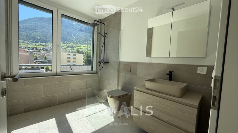 Modern bathroom with large windows offering a scenic mountain view, featuring a toilet, sink, mirror, and a glass-enclosed shower area.