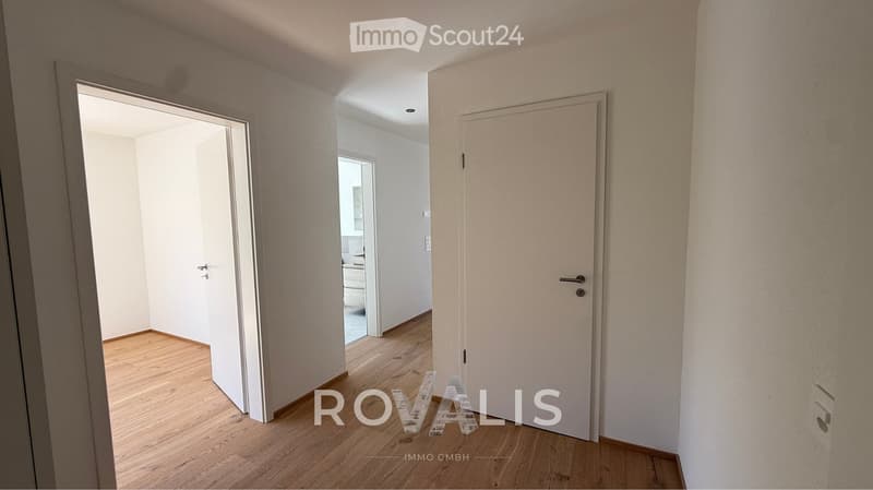 Empty hallway with wooden flooring, white walls, and open doors leading to other rooms.