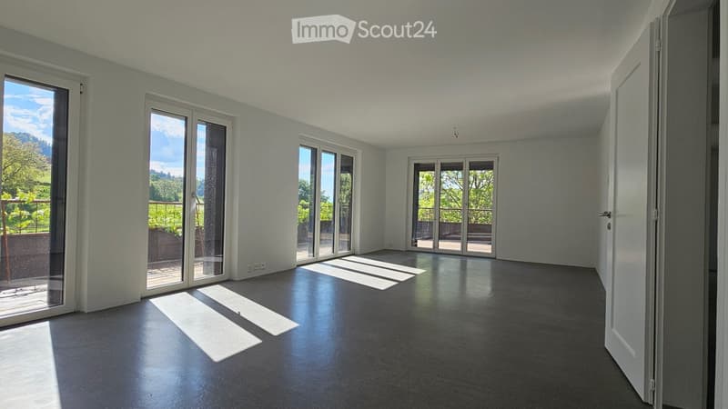 Empty room with large windows and sliding glass doors leading to a balcony, featuring a dark floor and white walls.