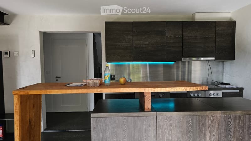Modern kitchen with dark wooden cabinets, stainless steel appliances, and a wooden island topped with a bottle, an apple, and other small items.