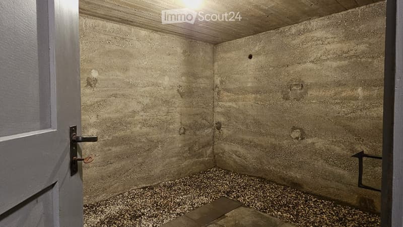 Empty room with concrete walls and a gravel floor, featuring a single door with a metal handle.