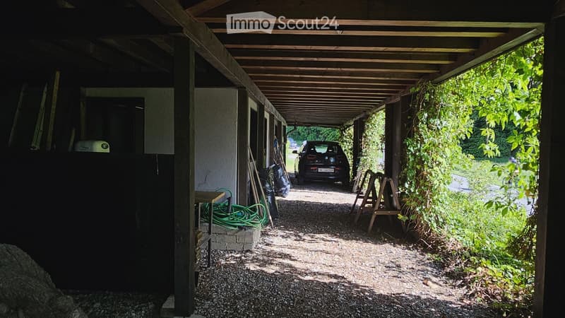 {"type": "Garage", "objects": [], "description": "Carport with wooden roof and concrete walls, containing a parked car, tools, and a small table.", "localized_descriptions": {"EN": "Carport with wooden roof and concrete walls, containing a parked car, too