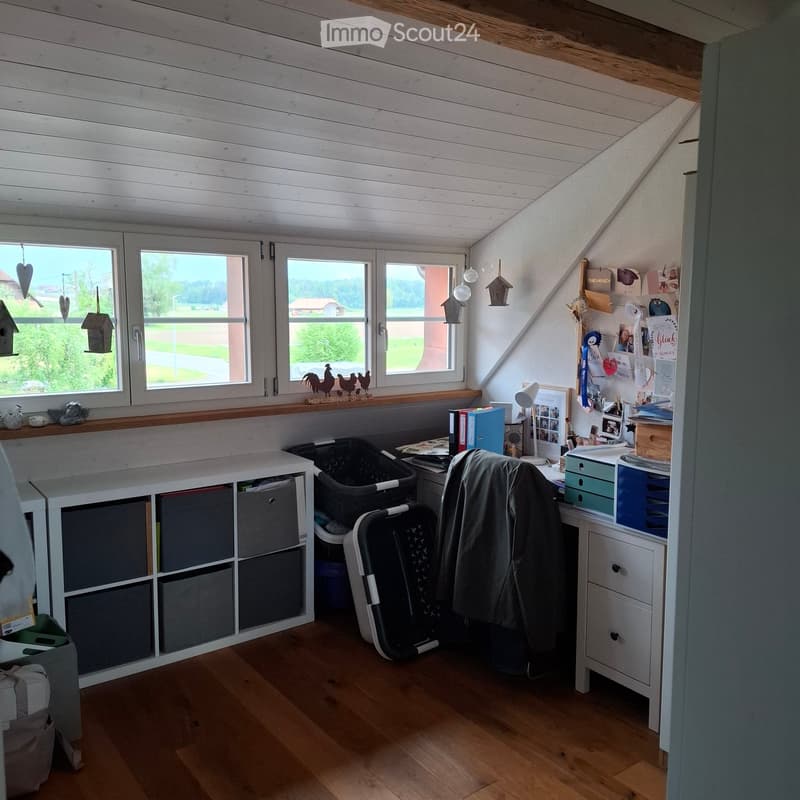 Furnished Room. Bright attic room with wooden floors, large windows, a desk with a chair, storage unit, and various decorative items.