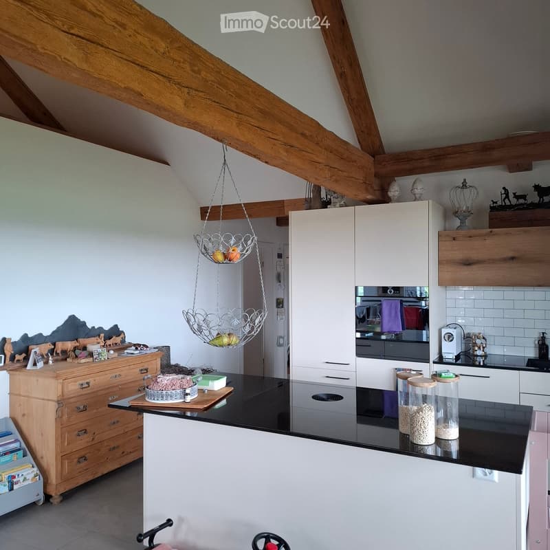 Kitchen. Modern kitchen with wooden beams, black countertops, white cabinets, hanging fruit baskets, and a central island.