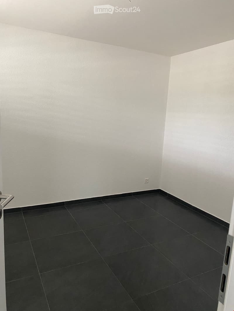 Empty room with white walls and black tiled floor, featuring a door frame and a visible electrical outlet.