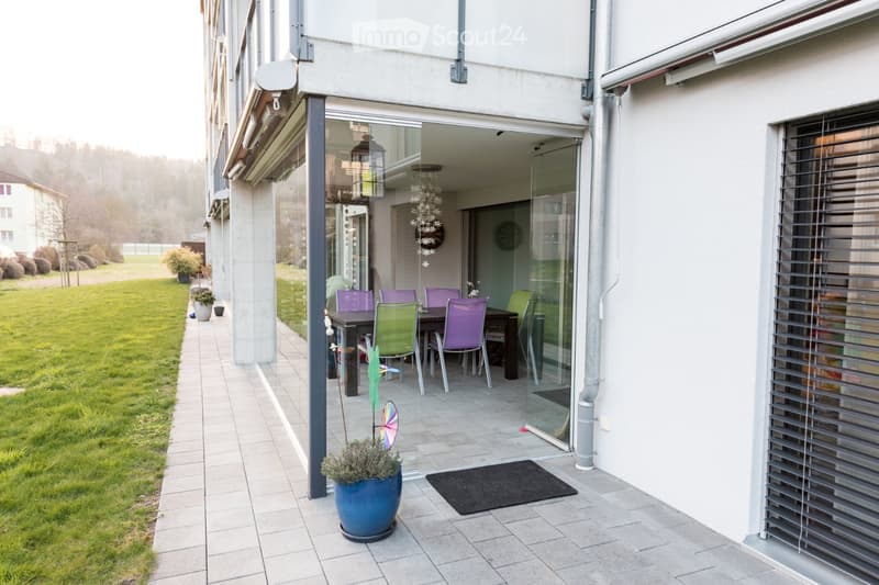 Balcony with a dining table and chairs, potted plants, and a view of a grassy area.