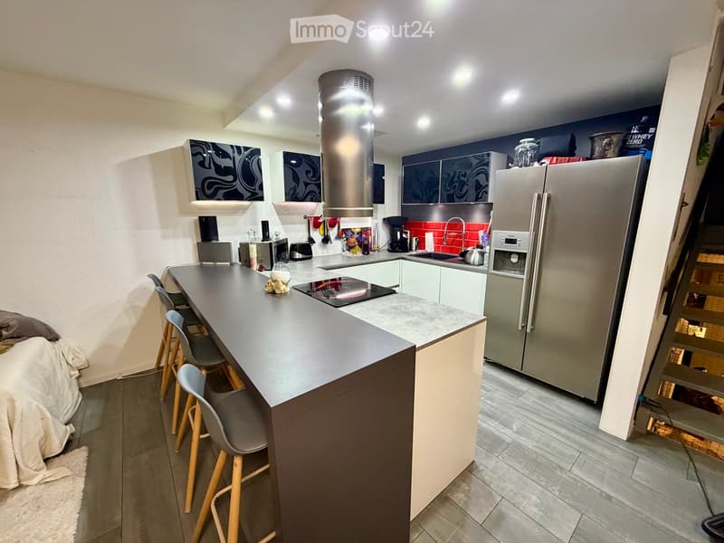 Modern kitchen with a central island, bar stools, stainless steel appliances, and a red backsplash.