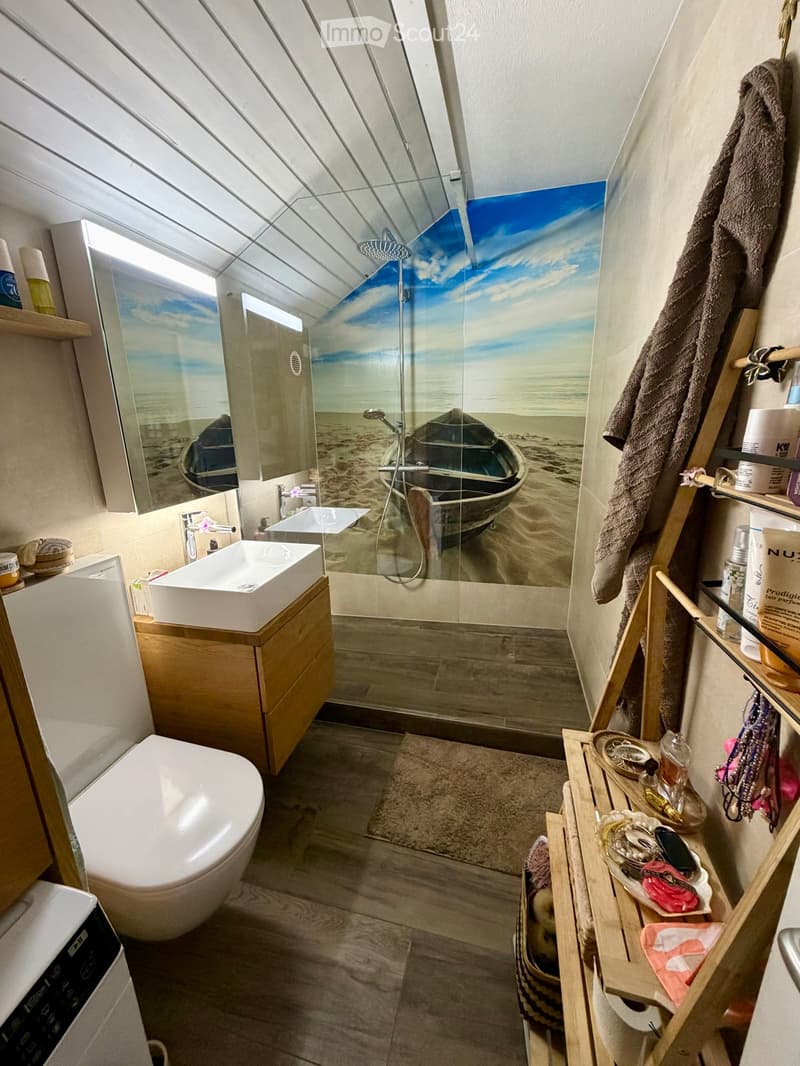 Modern bathroom with a large shower area featuring a beach-themed mural, a white sink, a toilet, and a wooden shelf holding towels and toiletries.