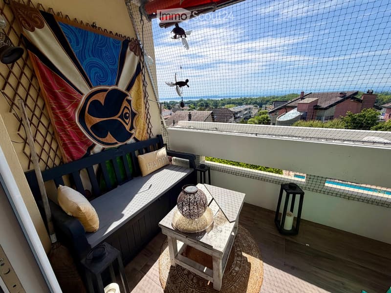 Balcony with a bench, small table, and decorative items, offering a scenic view of the ocean and surrounding area.