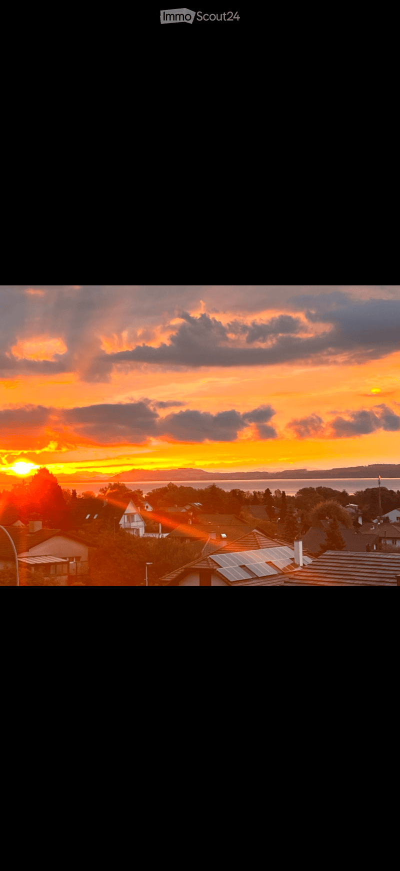 Residential neighborhood with houses, solar panels on roofs, and a scenic sunset view over a body of water.