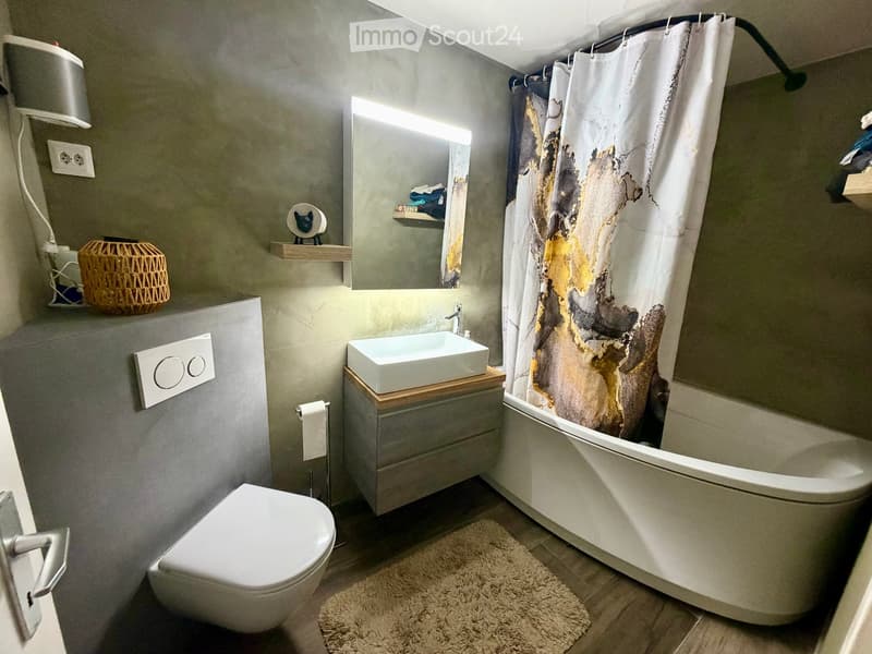 Modern bathroom with a white toilet, bathtub, sink, and mirror. Features a decorative wicker basket on a shelf and a stylish shower curtain with an abstract design.