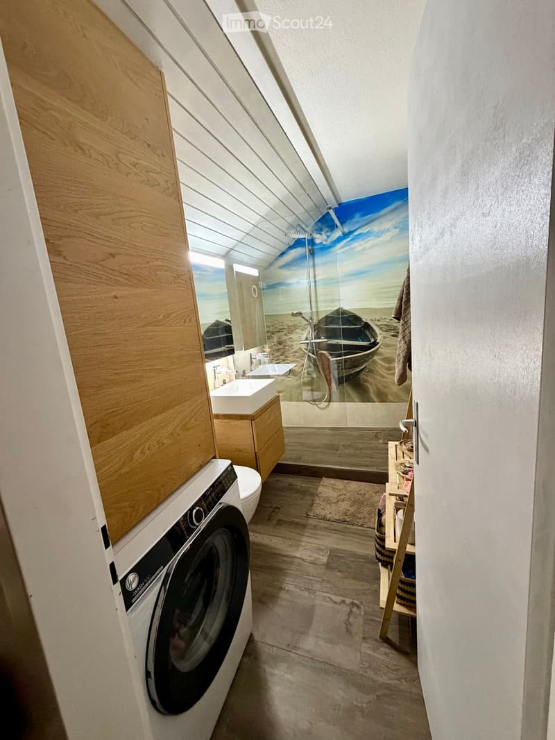Modern bathroom with a skylight, wooden cabinetry, a shower with a beach mural, a sink, toilet, and a private washing machine.